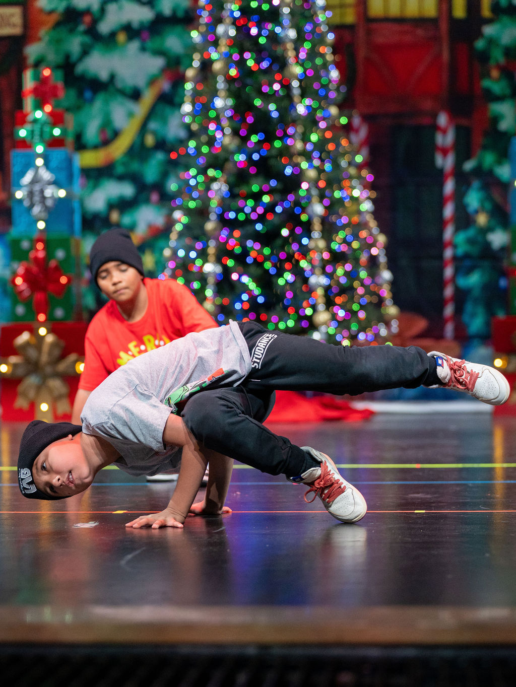 A breaking dancer holds a freeze beside the Christmas tree