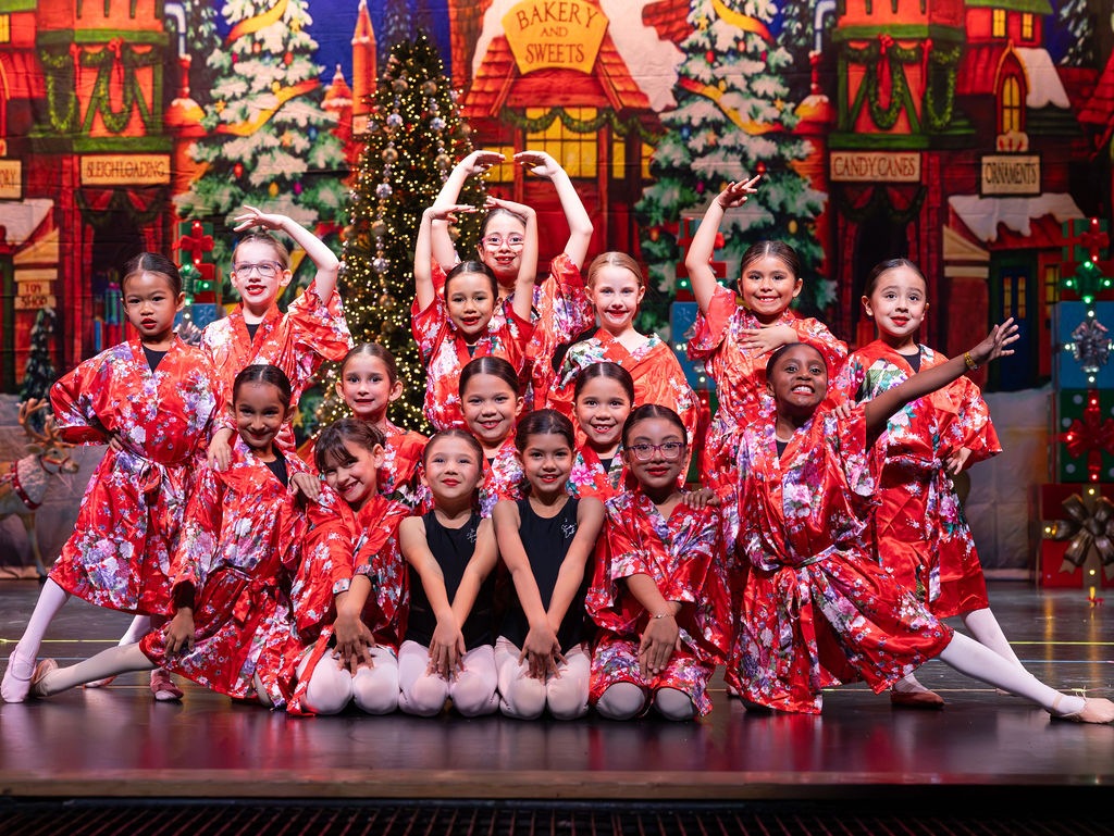 A group of young ballet dancers pose together in red holiday outfits